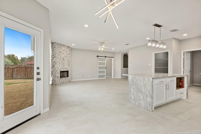 kitchen with a barn door, arched walkways, hanging light fixtures, a fireplace, and white cabinetry