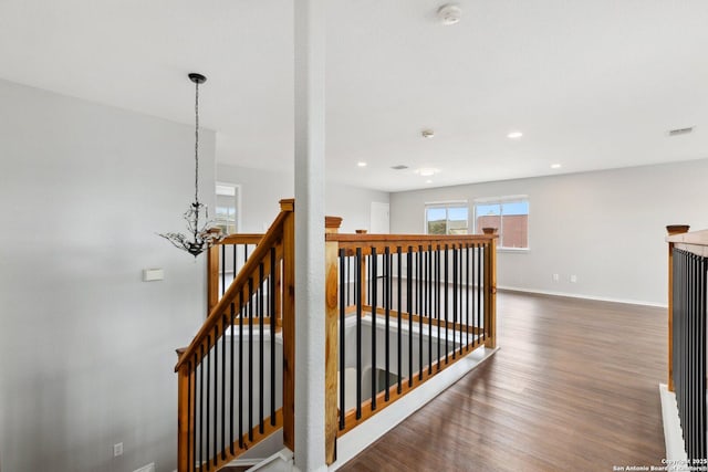 hall featuring a chandelier, dark wood-type flooring, an upstairs landing, visible vents, and baseboards