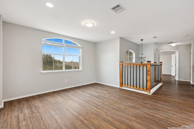 unfurnished room featuring dark wood-style floors, an inviting chandelier, visible vents, and baseboards