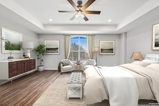 bedroom with a tray ceiling, recessed lighting, wood finished floors, and baseboards