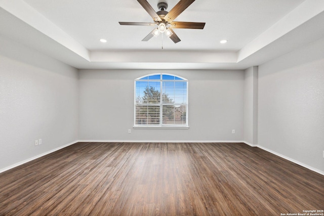 unfurnished room with a tray ceiling, dark wood-style flooring, a ceiling fan, and baseboards