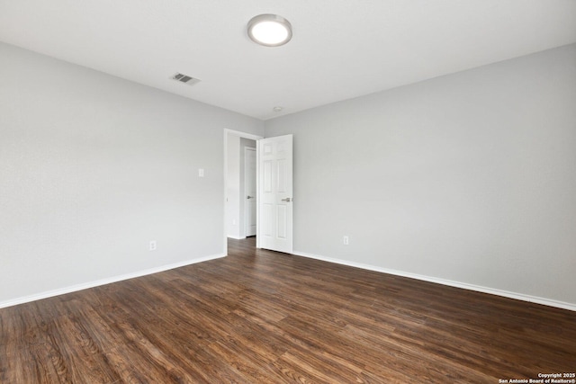 empty room with dark wood finished floors, visible vents, and baseboards