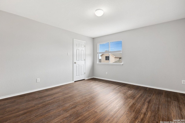 spare room featuring dark wood-style floors and baseboards