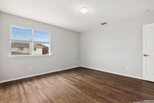 spare room with dark wood finished floors, visible vents, and baseboards