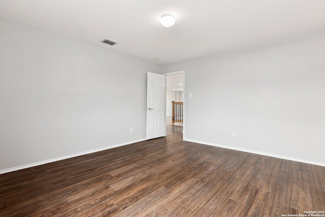 spare room featuring dark wood-style floors, visible vents, and baseboards