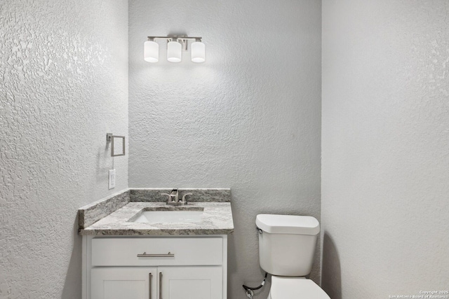 bathroom featuring toilet, vanity, and a textured wall