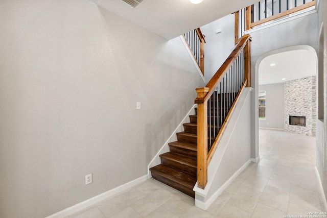 staircase featuring a large fireplace, tile patterned floors, arched walkways, and baseboards