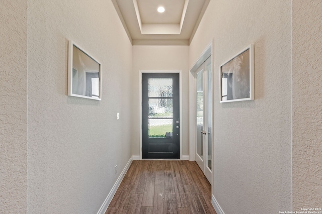 entryway with a tray ceiling, a textured wall, baseboards, and wood finished floors