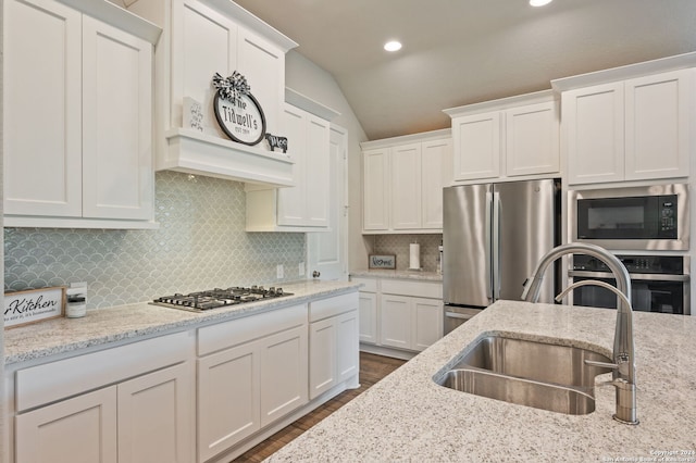 kitchen with light stone counters, stainless steel appliances, white cabinets, vaulted ceiling, and a sink