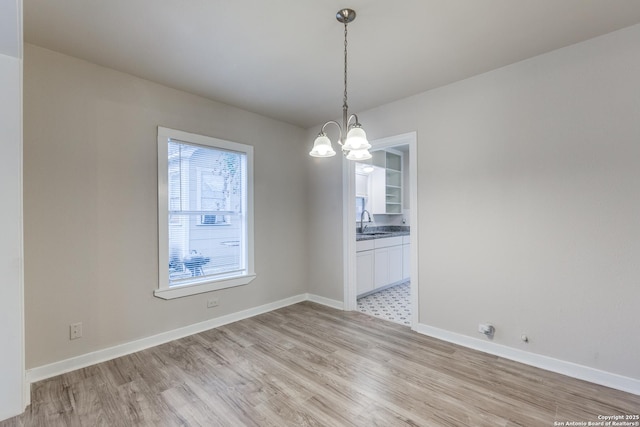 unfurnished dining area with a chandelier, baseboards, a sink, and light wood finished floors