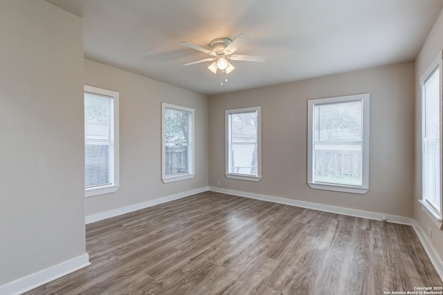 empty room featuring plenty of natural light, wood finished floors, a ceiling fan, and baseboards