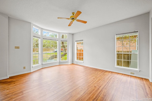 empty room with light wood-style floors, ceiling fan, baseboards, and a textured ceiling