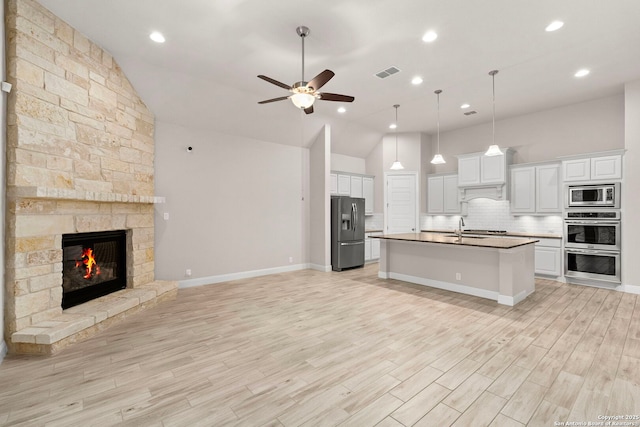 kitchen featuring stainless steel appliances, open floor plan, white cabinets, a sink, and an island with sink