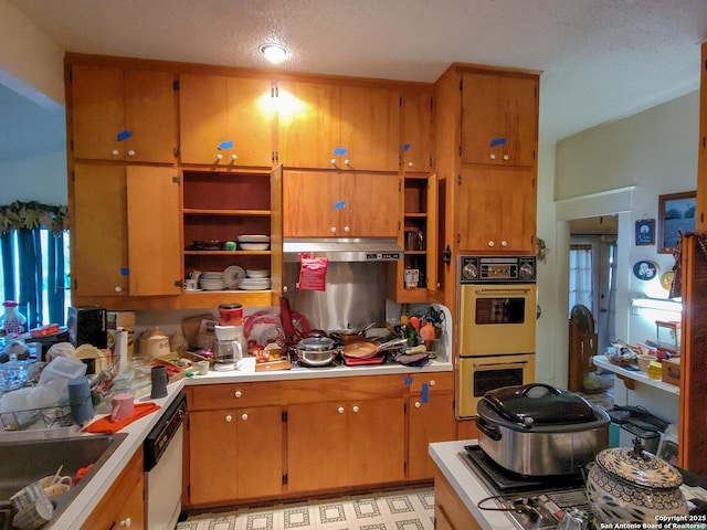 kitchen featuring dishwasher, brown cabinets, multiple ovens, light countertops, and a sink