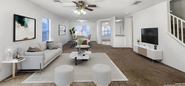 living room with stairway, visible vents, dark colored carpet, and a ceiling fan