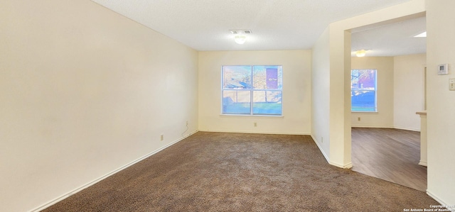 spare room featuring a textured ceiling, dark carpet, visible vents, and baseboards