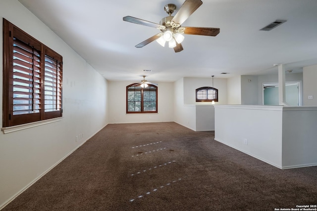 empty room featuring ceiling fan, visible vents, dark carpet, and baseboards