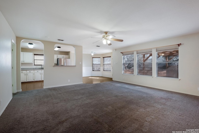 unfurnished living room with baseboards, dark carpet, visible vents, and a ceiling fan