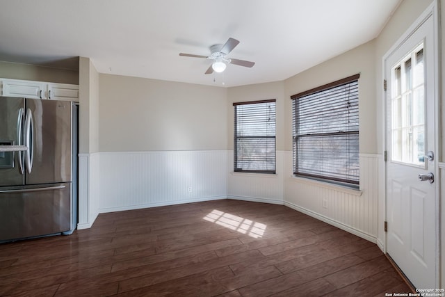 unfurnished dining area featuring dark wood-style floors, ceiling fan, and a wainscoted wall