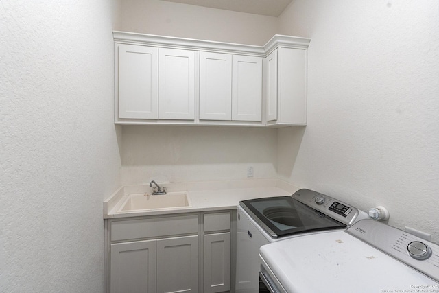 washroom featuring cabinet space, separate washer and dryer, a sink, and a textured wall