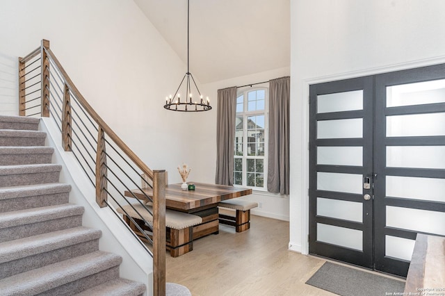 foyer featuring french doors, high vaulted ceiling, stairway, light wood-style floors, and a chandelier