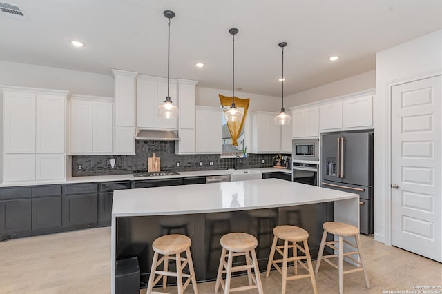 kitchen with appliances with stainless steel finishes, a center island, range hood, light countertops, and white cabinetry