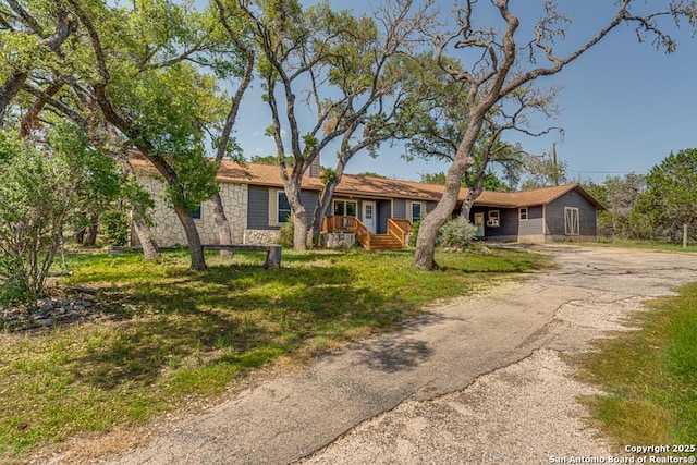 single story home featuring driveway, stone siding, and a front lawn