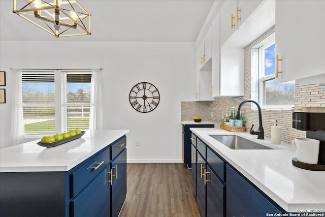 kitchen with white cabinets, blue cabinets, light countertops, pendant lighting, and a sink