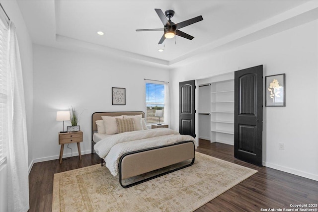 bedroom featuring dark wood-type flooring, a tray ceiling, and baseboards