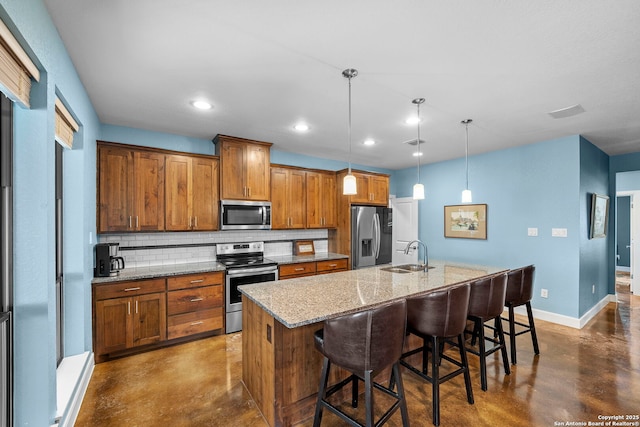 kitchen with brown cabinetry, finished concrete flooring, an island with sink, a sink, and appliances with stainless steel finishes