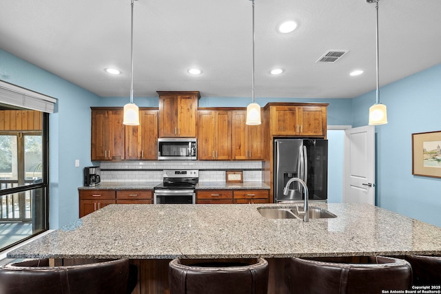 kitchen featuring visible vents, brown cabinets, a sink, tasteful backsplash, and stainless steel appliances