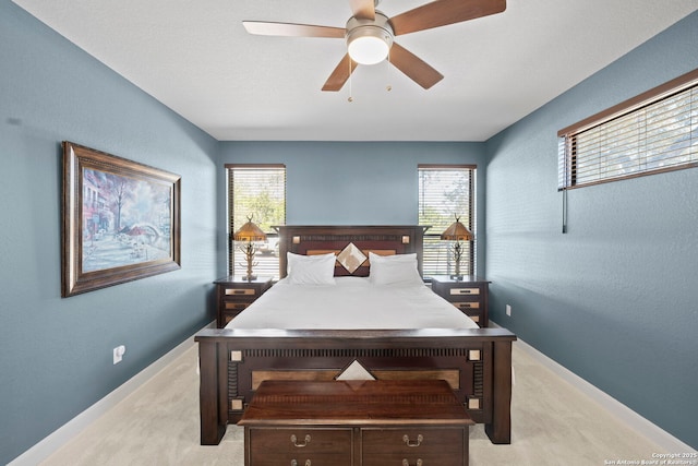 bedroom with ceiling fan, a textured wall, baseboards, and light carpet