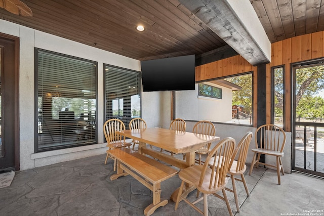 dining space with wooden ceiling, wooden walls, a healthy amount of sunlight, and concrete flooring