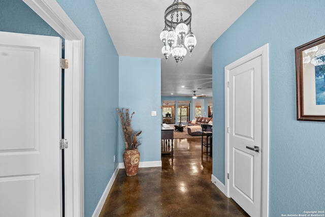 hallway with baseboards, concrete flooring, and an inviting chandelier