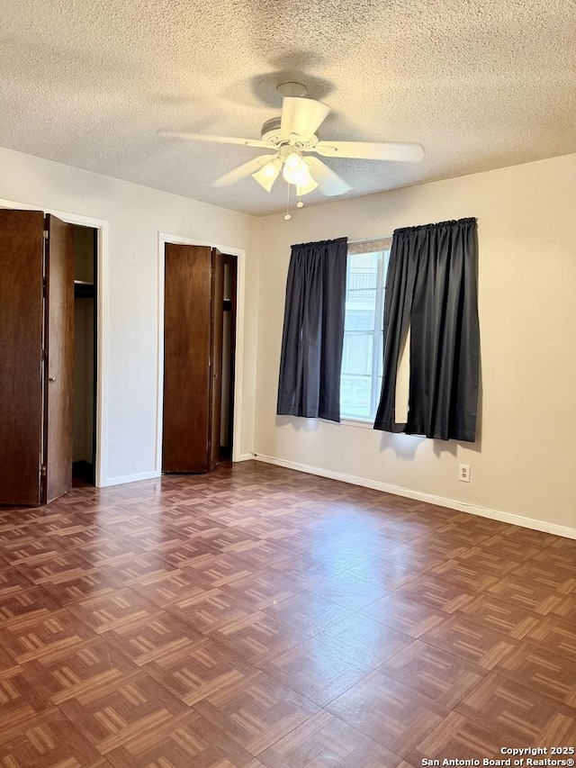 unfurnished bedroom with ceiling fan, a textured ceiling, baseboards, and two closets