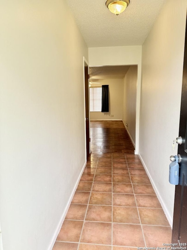 corridor with a textured ceiling, tile patterned flooring, and baseboards