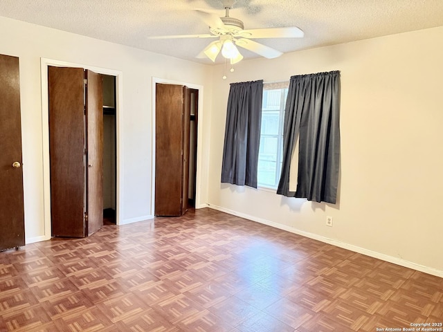 unfurnished bedroom featuring a textured ceiling, baseboards, and two closets