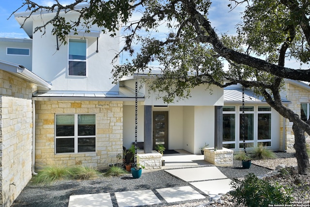 back of house featuring metal roof, a standing seam roof, stone siding, and stucco siding