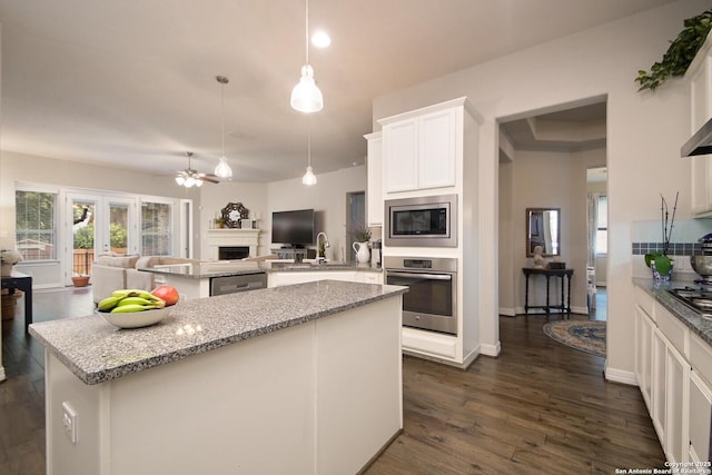 kitchen featuring open floor plan, a center island, decorative light fixtures, light stone countertops, and stainless steel appliances