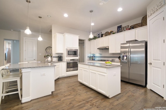 kitchen featuring stainless steel appliances, hanging light fixtures, an island with sink, and light stone countertops