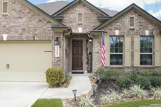 property entrance with a garage, brick siding, and roof with shingles