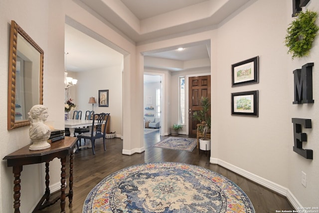 entrance foyer with a notable chandelier, dark wood finished floors, and baseboards