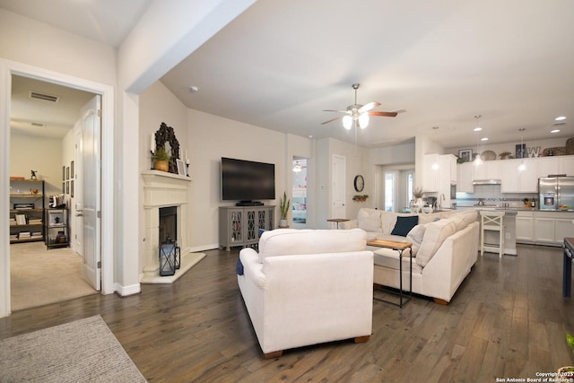 living room with a fireplace with raised hearth, recessed lighting, dark wood-style flooring, visible vents, and a ceiling fan