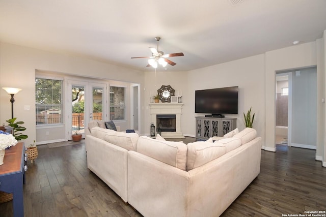 living area with french doors, dark wood finished floors, a fireplace with raised hearth, ceiling fan, and baseboards