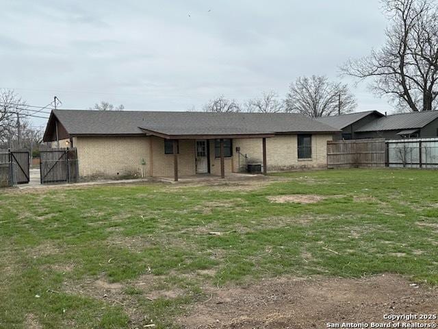 back of property featuring a gate, fence, a lawn, and brick siding