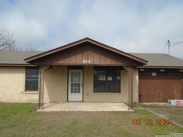 single story home with a shingled roof, a front yard, a patio area, and brick siding