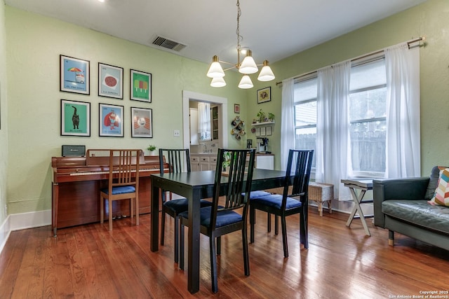 dining space with baseboards, wood finished floors, visible vents, and an inviting chandelier