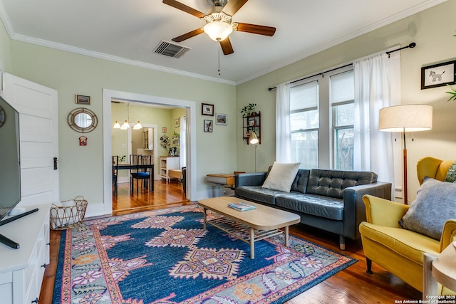 living area with ceiling fan with notable chandelier, wood finished floors, visible vents, baseboards, and ornamental molding