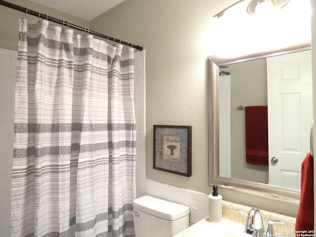 bathroom with toilet, a textured wall, a shower with shower curtain, and vanity