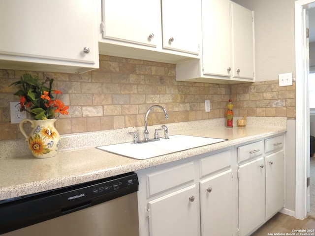 kitchen with tasteful backsplash, white cabinets, dishwasher, light countertops, and a sink